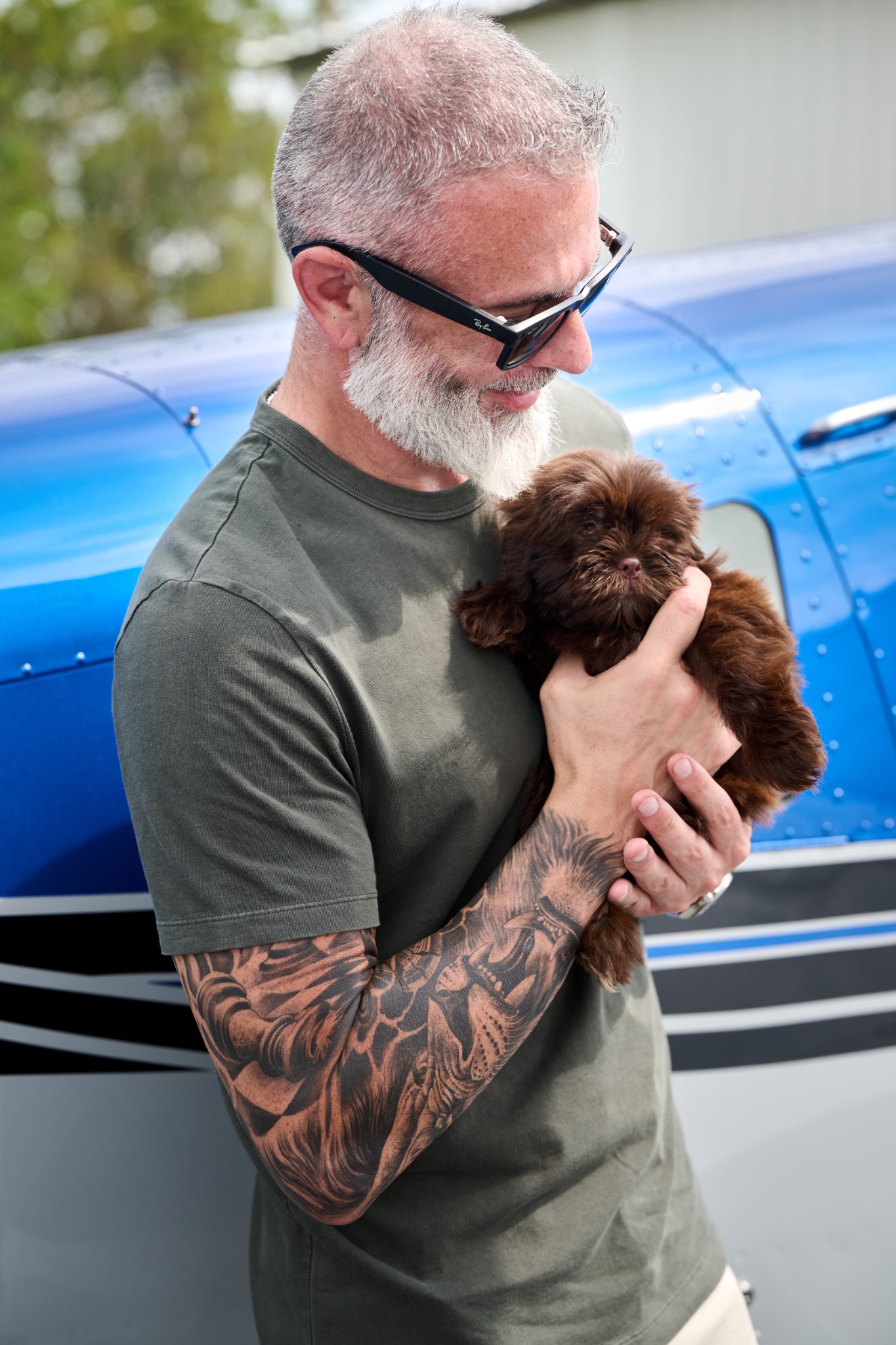Ed Foley holding a small brown dog beside a blue airplane